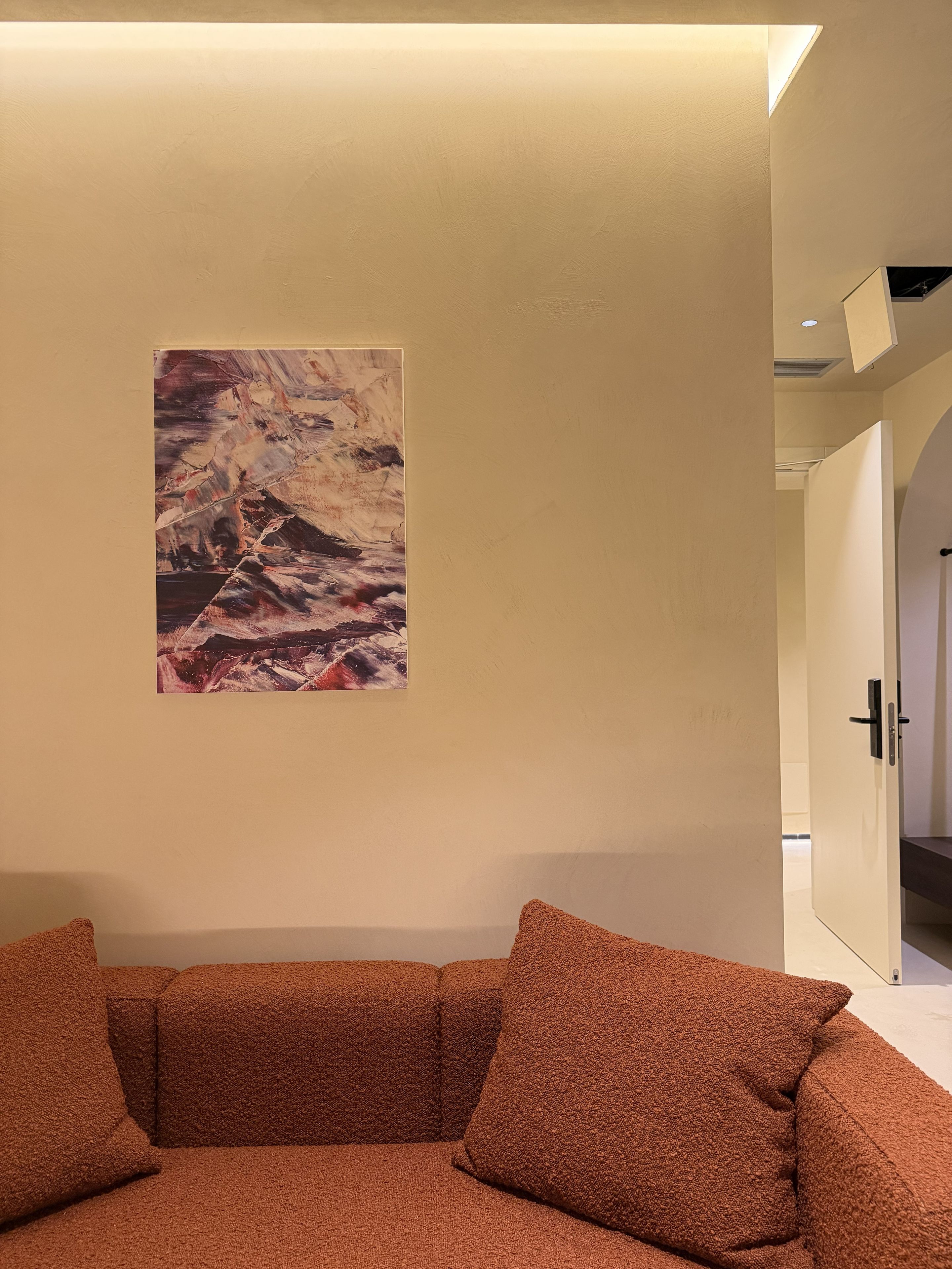 Een modern interieur met een beige muur, een groot abstract schilderij en een bruine sofa met structuur.