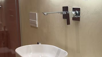 A bathroom with a white vessel sink, a towel rack with folded towels, and a mirror with a wavy design.