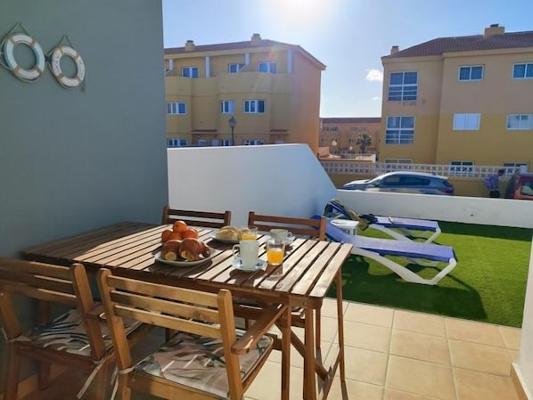 Un balcon avec une table préparée pour le petit-déjeuner, une vue sur les immeubles et une petite pelouse.