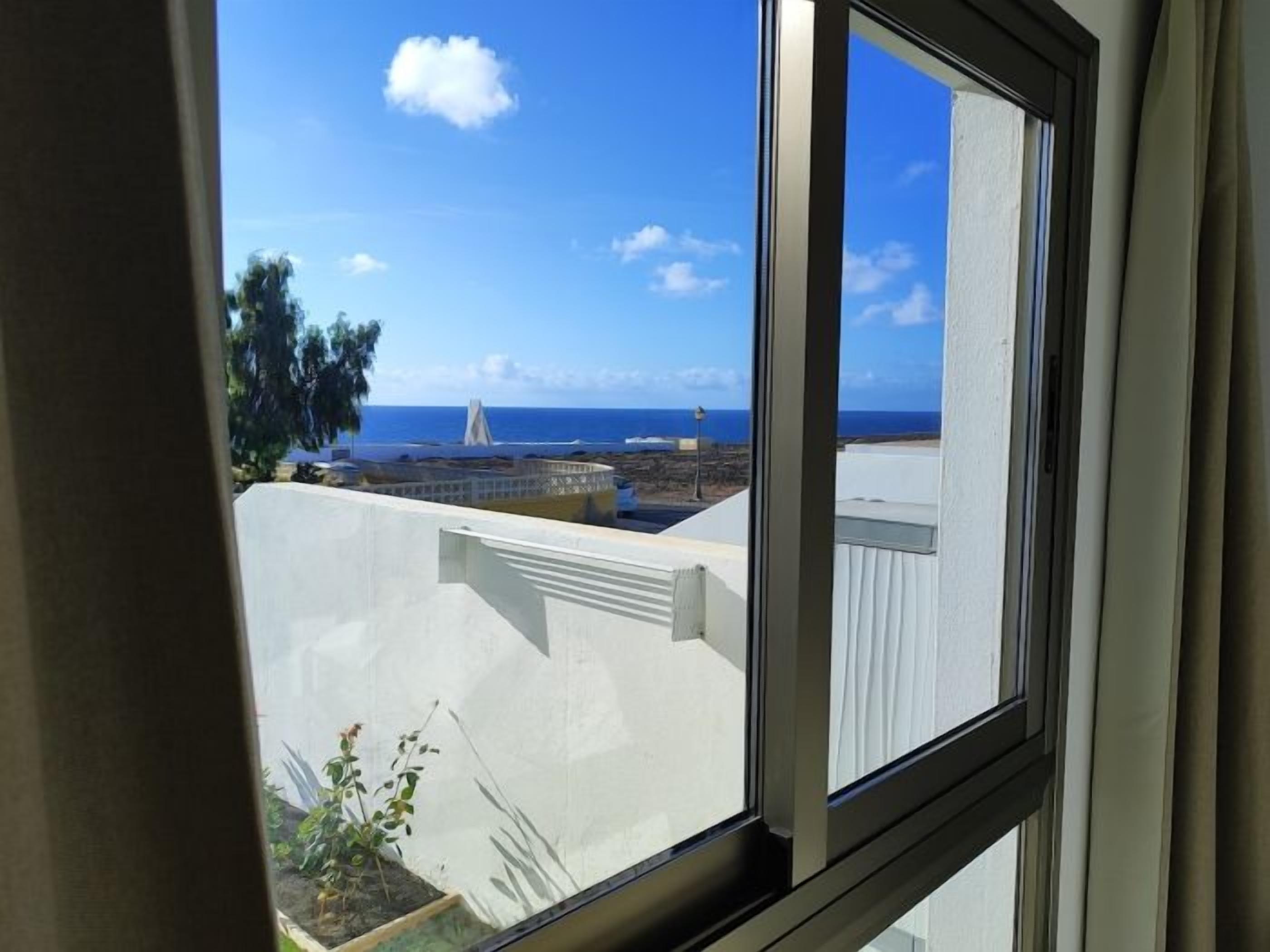 A view through a window with a clear sky, a distant coastline, and a building with a white exterior.