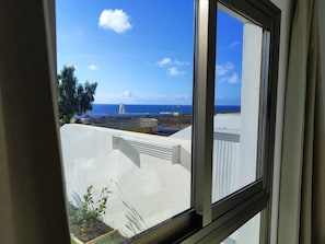 Une vue à travers une fenêtre, avec un ciel dégagé, une côte lointaine et un bâtiment à la façade blanche.