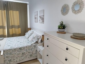 A bedroom with a bed, a dresser, a nightstand, a window with curtains, and wall decor. - Ares Holiday Home in the heart of the island (Costa Antigua)
