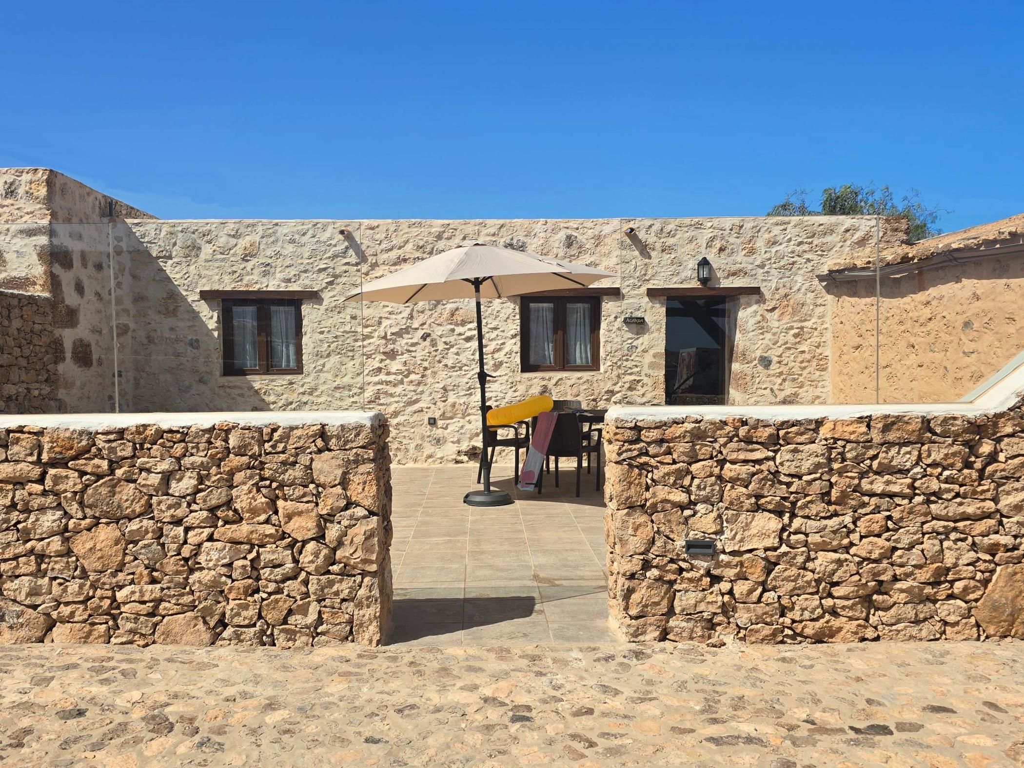 A stone building with a patio area, a table with chairs, and an umbrella.