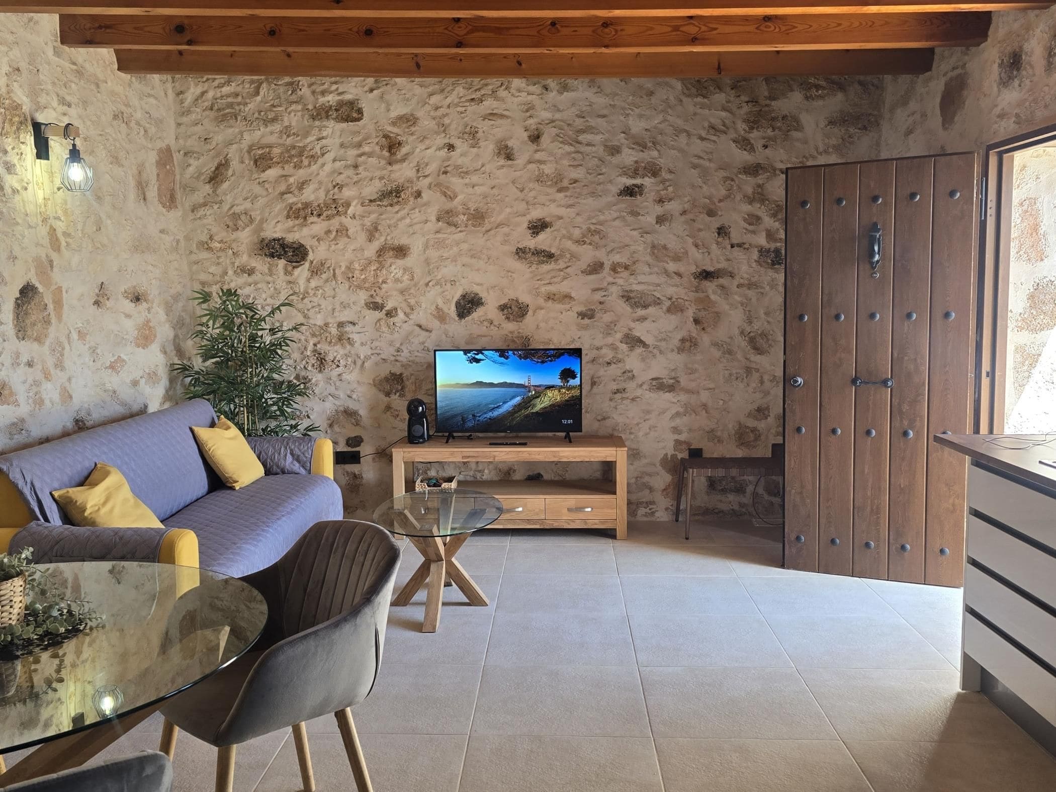 Un salon chaleureux avec un mur en pierre, un canapé, une table basse en verre et un téléviseur.