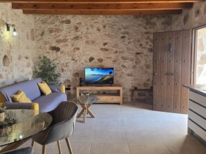 A cozy living room with a stone wall, a sofa, a glass coffee table, and a television. - Aganda Tefía Suites – Holiday Apartment (Tefía)