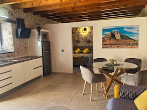 Eine moderne Küche mit integriertem Mikrowellenherd und Kühlschrank, ein Essbereich mit Glastisch und Stühlen sowie ein Schlafzimmer mit Bett und einem Berg-Bild.