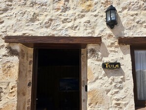 Ein Gebäude mit einem Schild, auf dem 'Tula' über einem Hauseingang steht, einem hölzernen Türrahmen und einem an der Wand befestigten Laternenaufsatz.