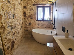 Ein Badezimmer mit Steinwand, einer freistehenden Badewanne, einem Fenster mit Vorhängen und einem modernen Waschbecken.