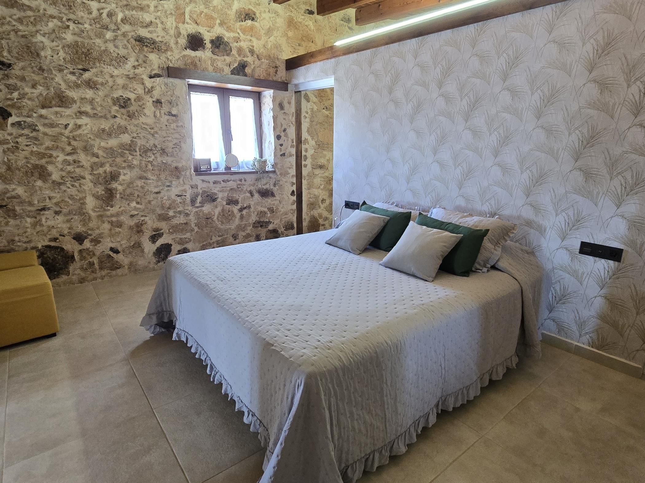 Ein Schlafzimmer mit einer Steinsandsteinwand, einem Bett mit weißer Bettdecke und einem Fenster mit Vorhängen.