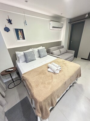 Une chambre d’hôtel comprenant un lit, un canapé, une petite table, un appareil de climatisation et une porte.