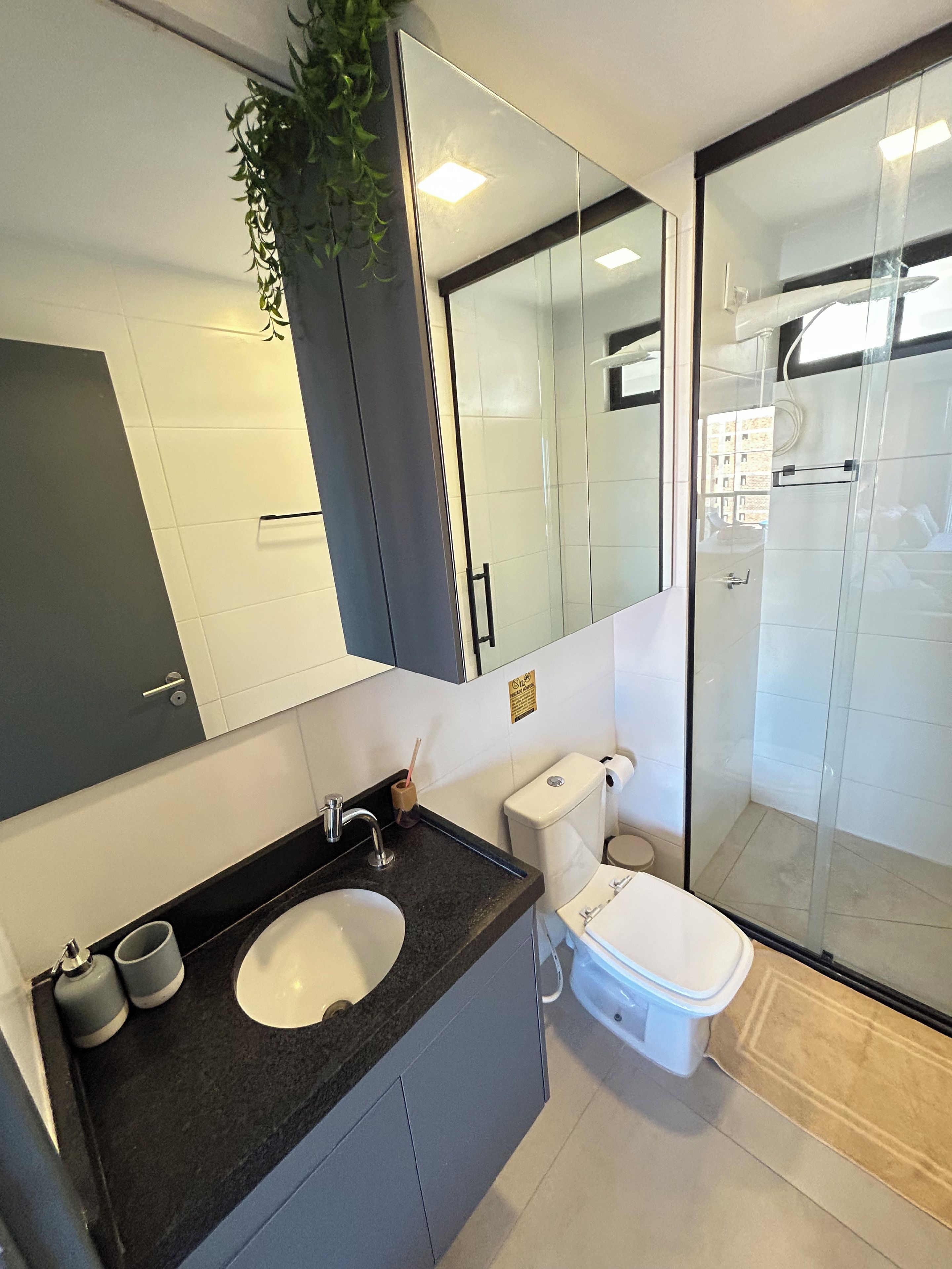 Casa de banho moderna com lavatório de bancada preta, sanita branca e cabine de duche em vidro.