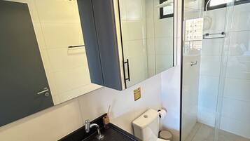 Casa de banho moderna com lavatório de bancada preta, sanita branca e cabine de duche em vidro.
