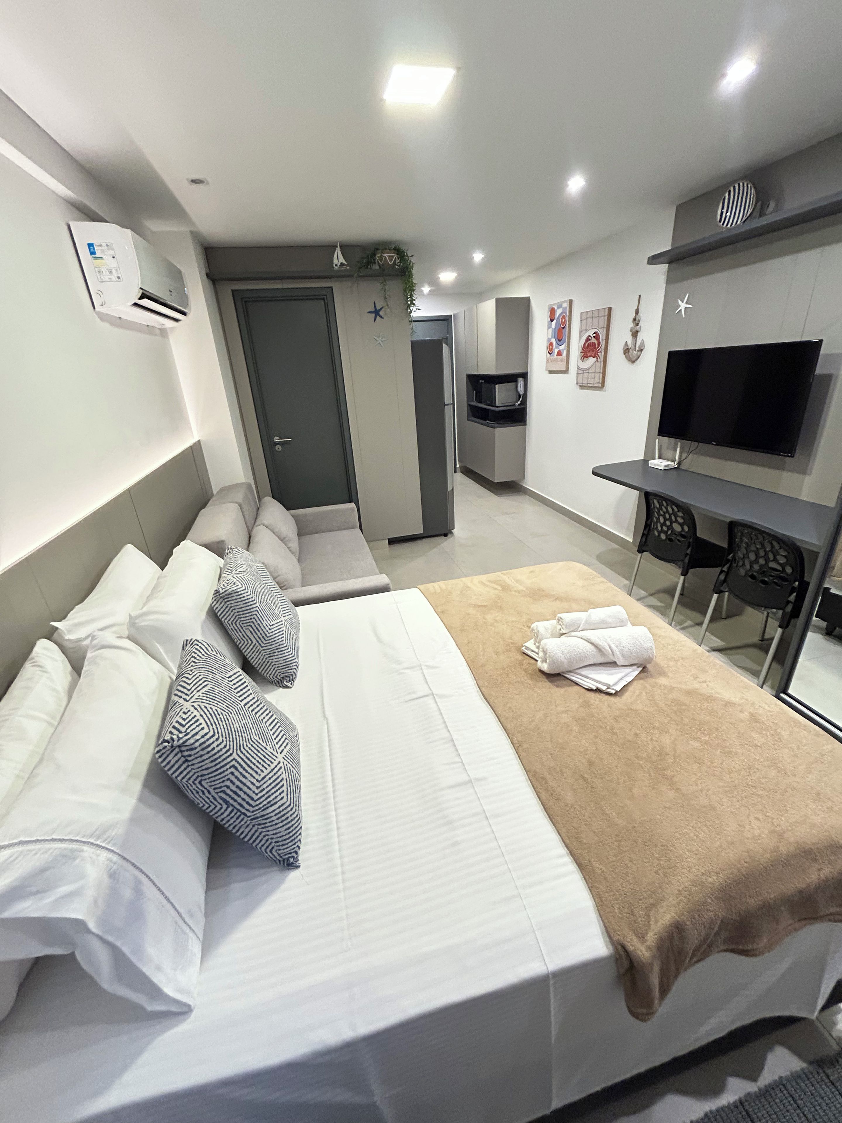 Quarto de hotel com cama, sofá, escrivaninha com televisão de tela plana, micro-ondas e geladeira.