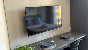 Uma sala de jantar moderna com televisão de tela plana na parede, uma mesa de jantar comprida com duas cadeiras e elementos decorativos como uma estrela e uma planta.
