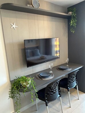 Uma sala de jantar moderna com televisão de tela plana na parede, uma mesa de jantar comprida com duas cadeiras e elementos decorativos como uma estrela e uma planta.