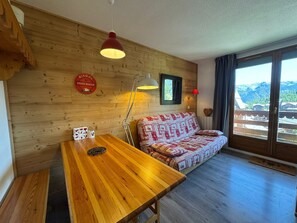 A cozy room with a wooden wall, a sofa, a table, and a view of mountains. - Appartement 6 pers avec balcon et vue sur le Queyras – Résidence Betelgeuse (Risoul)