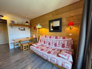 A cozy room with a wooden wall, a sofa with a patterned cover, a wooden table, and a bench. - Appartement 6 pers avec balcon et vue sur le Queyras – Résidence Betelgeuse (Risoul)