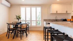 A modern kitchen with white cabinets, a wooden countertop, and a dining area with a table and chairs. - The Blue Door on Victoria (Footscray)