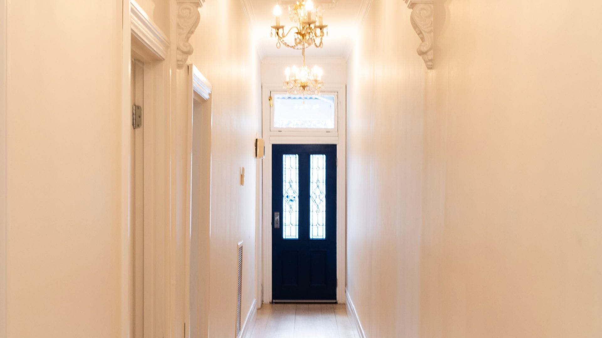 Ein Flur mit einer dunkelblauen Tür, weißen Wänden und einem Chandelier.