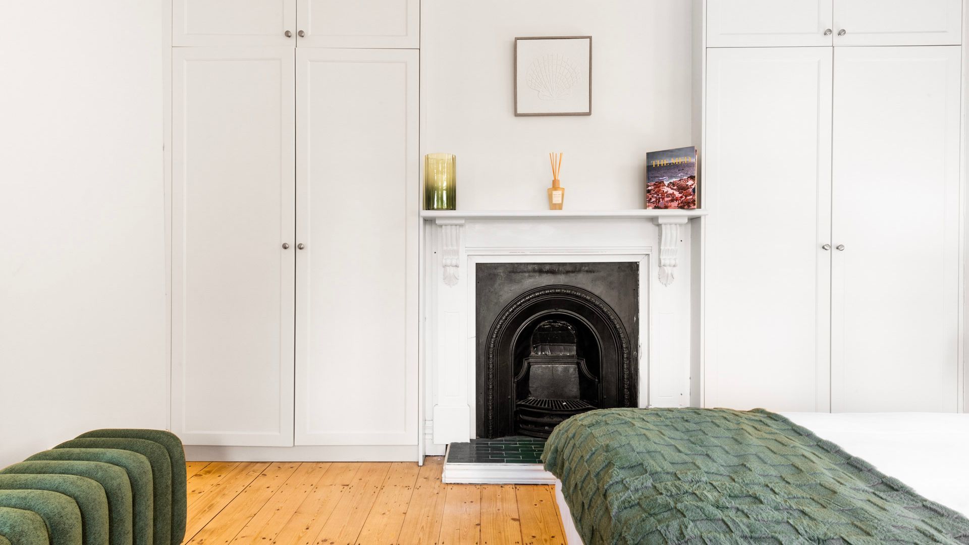 Een slaapkamer met een open haard, een bed, een groen gestoffeerde bank en een ingelijste foto aan de muur.