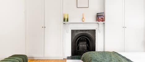 A bedroom with a fireplace, a bed, a green upholstered bench, and a framed picture on the wall.