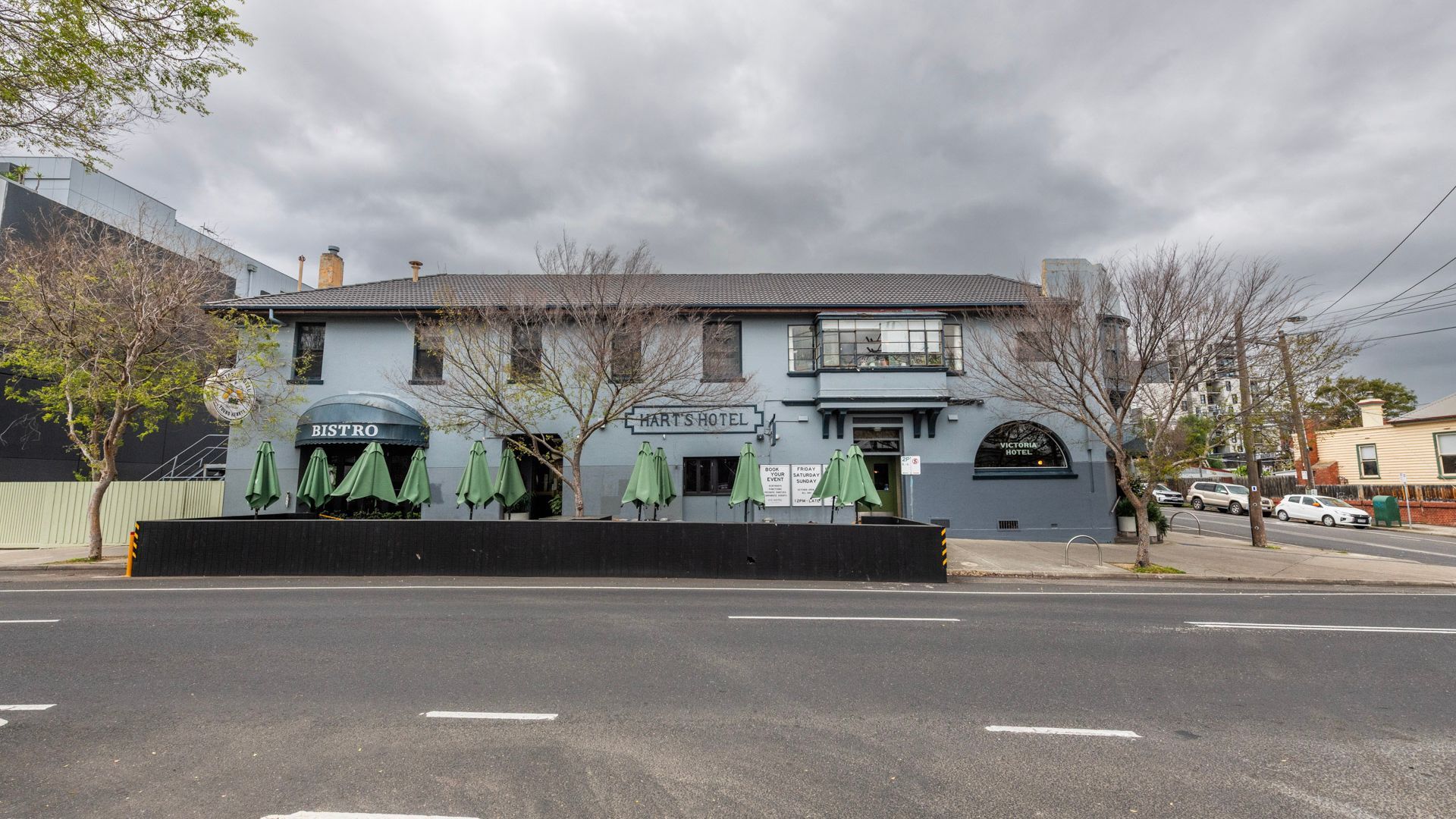 A two-story building with a sign for 'HART'S HOTEL' and 'BISTRO' on the ground floor. There are green umbrellas outside the windows.