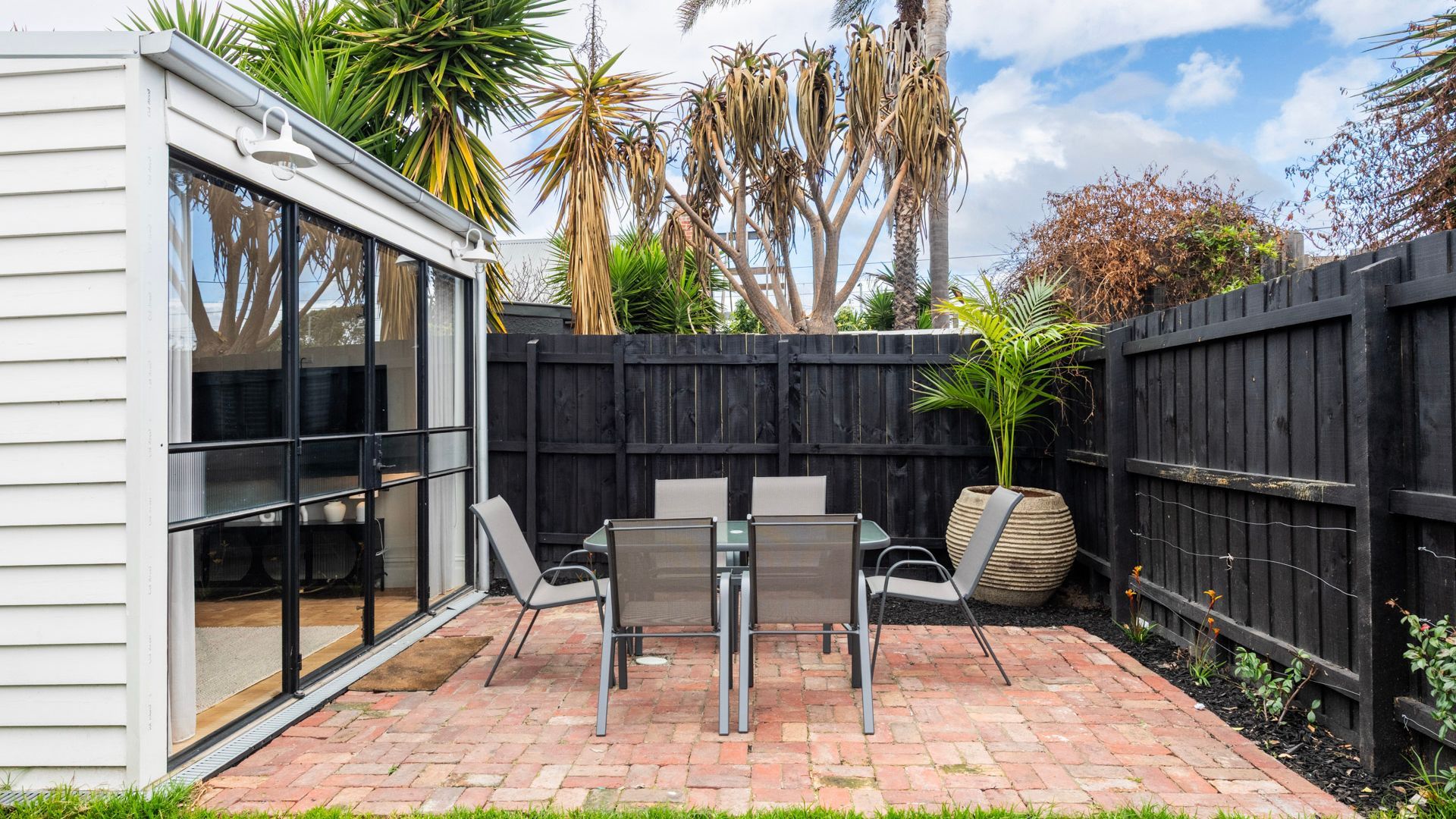A patio with a table and chairs, a potted plant, and a wooden fence.