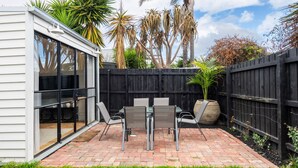 A patio with a table and chairs, a potted plant, and a wooden fence. - The Blue Door on Victoria (Footscray)