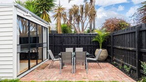 A patio with a table and chairs, a potted plant, and a wooden fence. - The Blue Door on Victoria (Footscray)