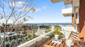 A balcony with a view of the sea, a table with a book and a cup, and a chair. - The Birdsnest Bondi (Waverley)