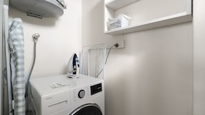 A compact laundry area with a washing machine, an iron, and a drying rack. - The Birdsnest Bondi (Waverley)