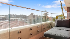 En balkon med sofa, kaktus og udsigt til bygninger.