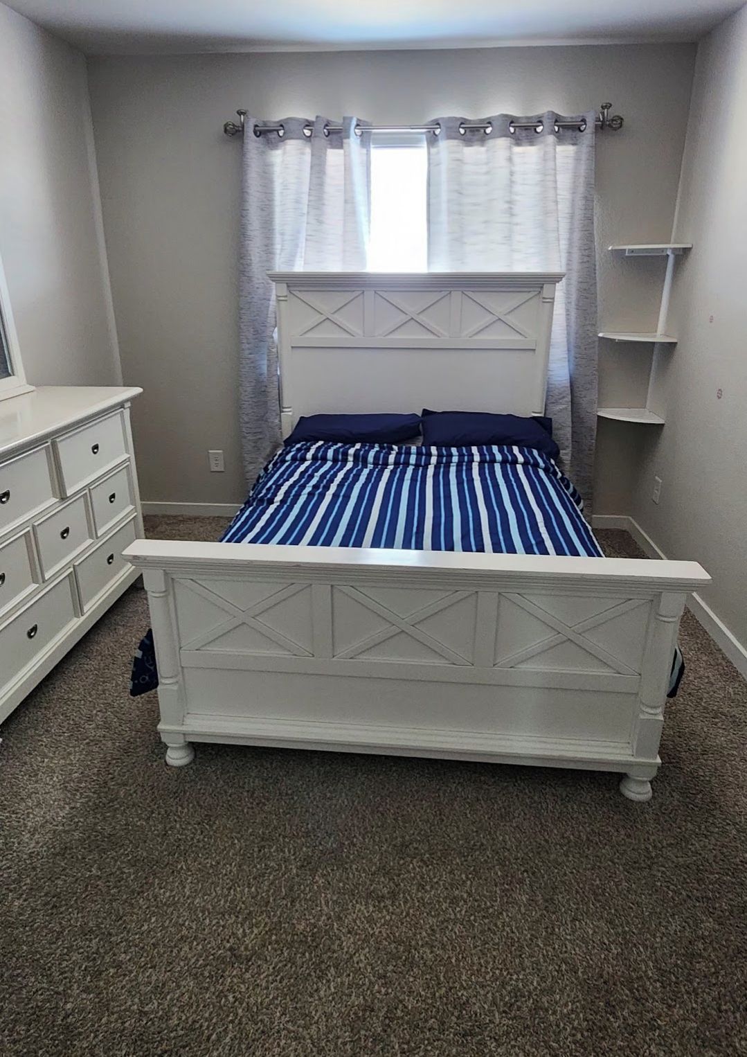 A bedroom with a bed, dresser, and shelving unit.