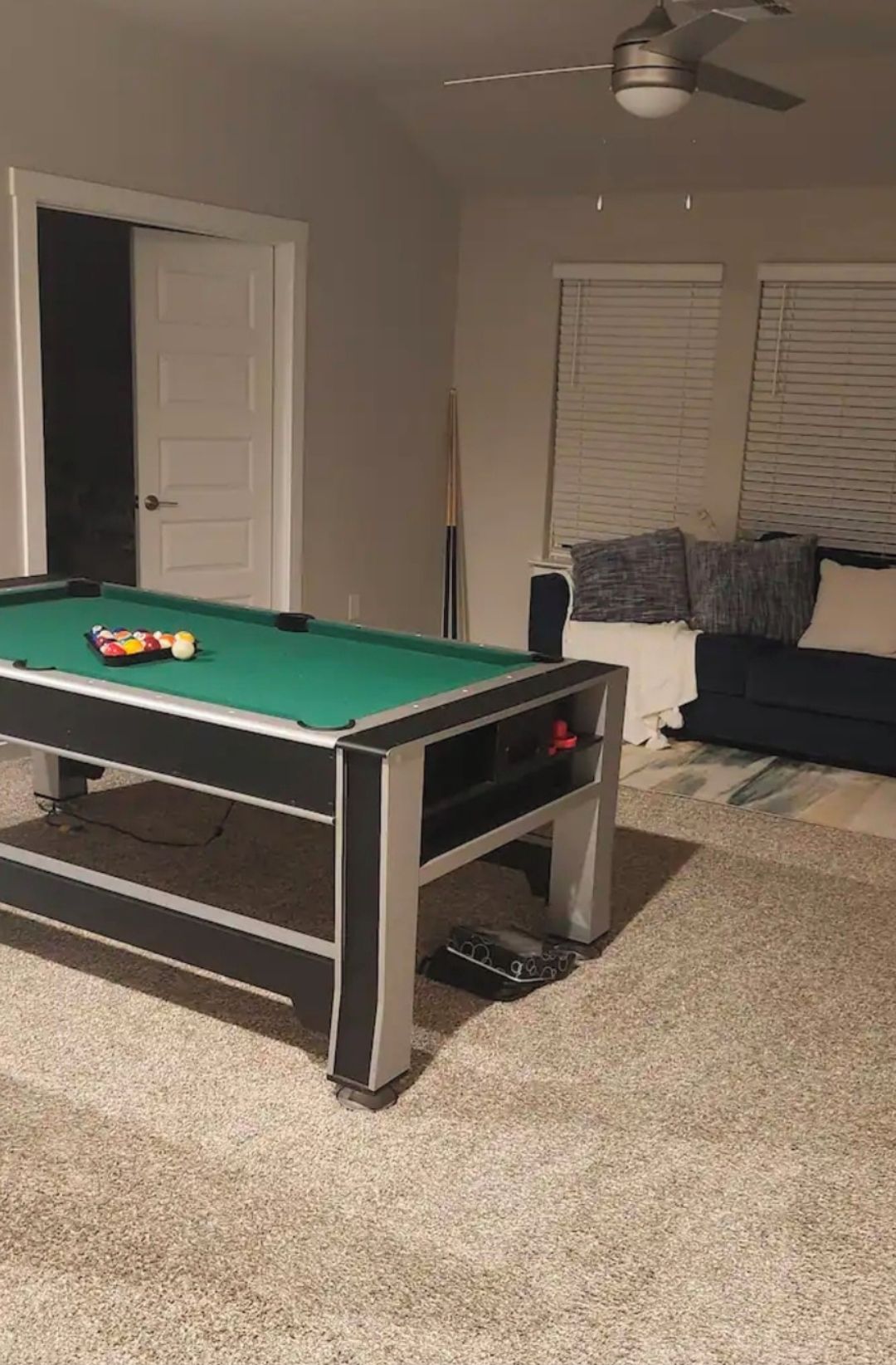 Une table de billard avec des billes, un ventilateur de plafond et un canapé dans une pièce dont le sol est recouvert de moquette.