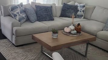 Een woonkamer met een beige bank, een houten salontafel en een vloerkleed met dessin.