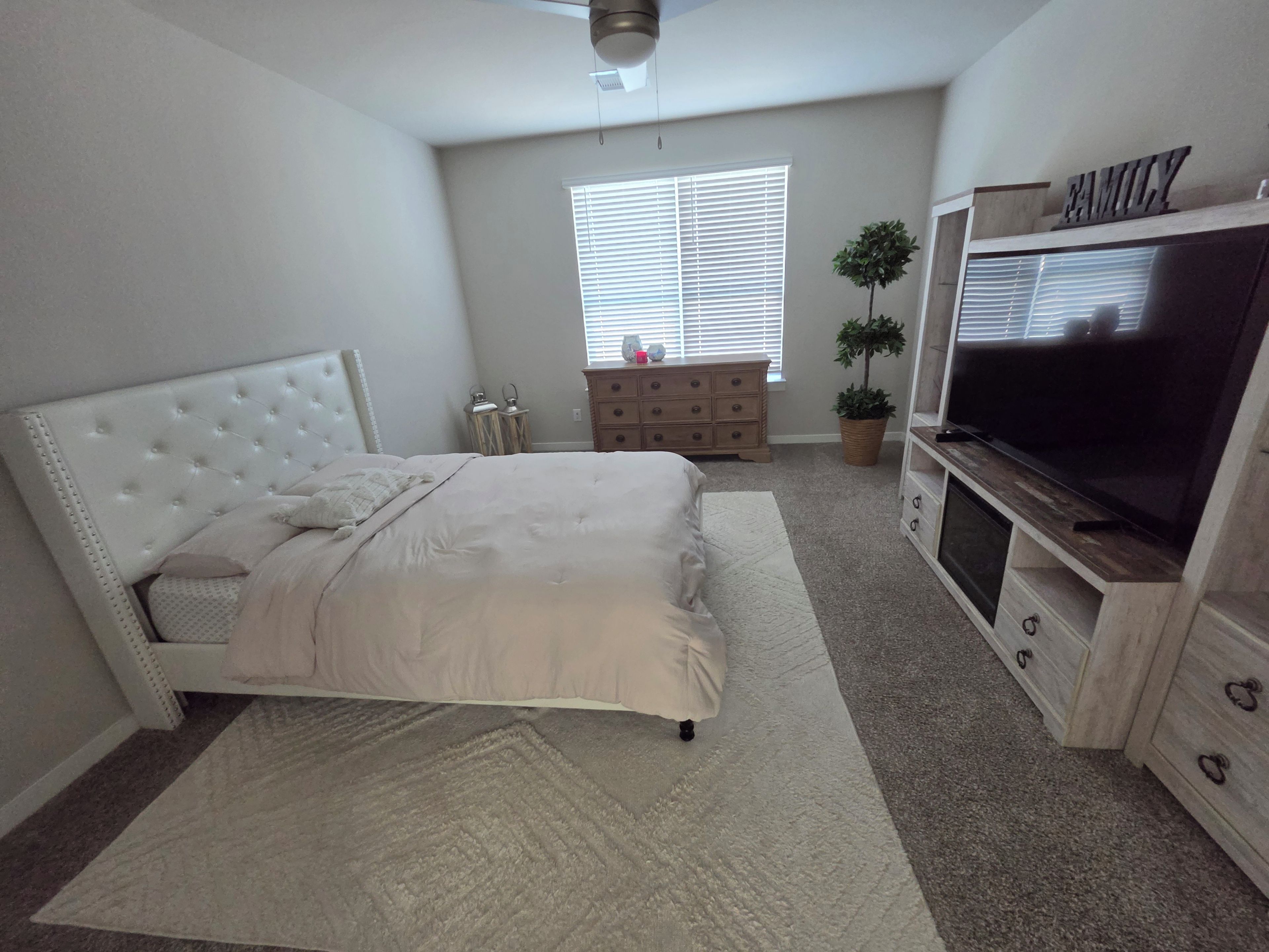 Ein Schlafzimmer mit Bett, Kommode, Fernseher und einem Fenster mit Jalousien.