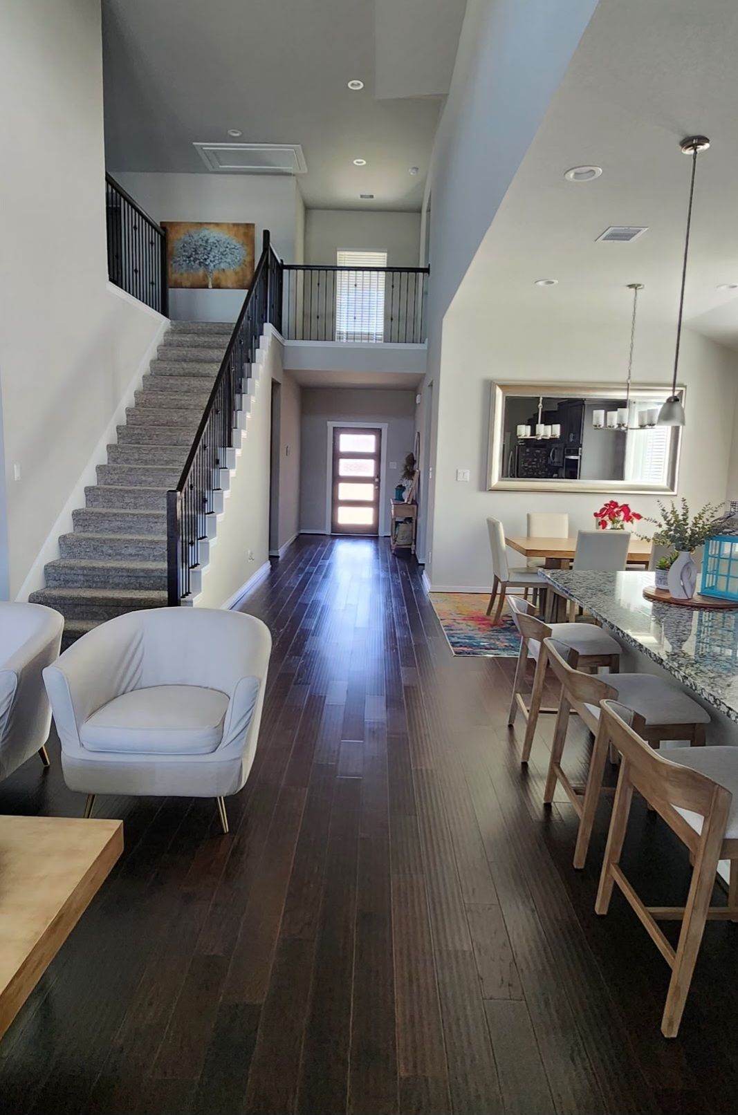 A spacious interior with a staircase leading to a second floor, a dining area with bar stools, and a kitchen with a large window.