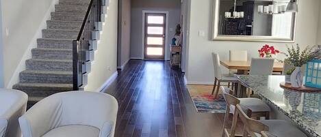A spacious interior with a staircase leading to a second floor, a dining area with bar stools, and a kitchen with a large window.