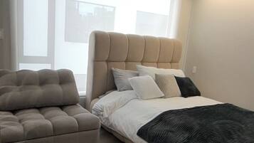 Et moderne soveværelse med seng, sofa og stort vindue.