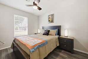 Ein Schlafzimmer mit einem Bett, Nachttischen, einem Deckenventilator, einem Fenster mit Jalousien und einem Poster an der Wand.
