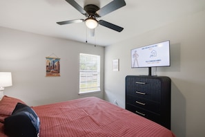 A bedroom with a bed, a ceiling fan, a TV on the wall, a window with blinds, and a poster on the wall. - Experience Route 66! Stay in this unique 3BR themed home featuring Chicago, Springfield, & Los Angeles-inspired bedrooms and a Tulsa-themed living room, a fenced yard, and private patio. (Broken Arrow)