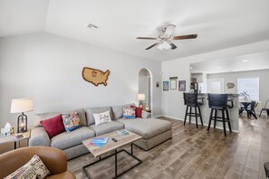 A modern living room with a sofa, coffee table, and a dining area with bar stools. - Experience Route 66! Stay in this unique 3BR themed home featuring Chicago, Springfield, & Los Angeles-inspired bedrooms and a Tulsa-themed living room, a fenced yard, and private patio. (Broken Arrow)