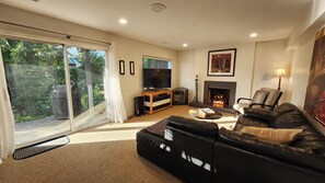 Ein Wohnzimmer mit Kamin, Fernseher, einer Couch und einer Glasschiebetür, die in einen Garten führt.