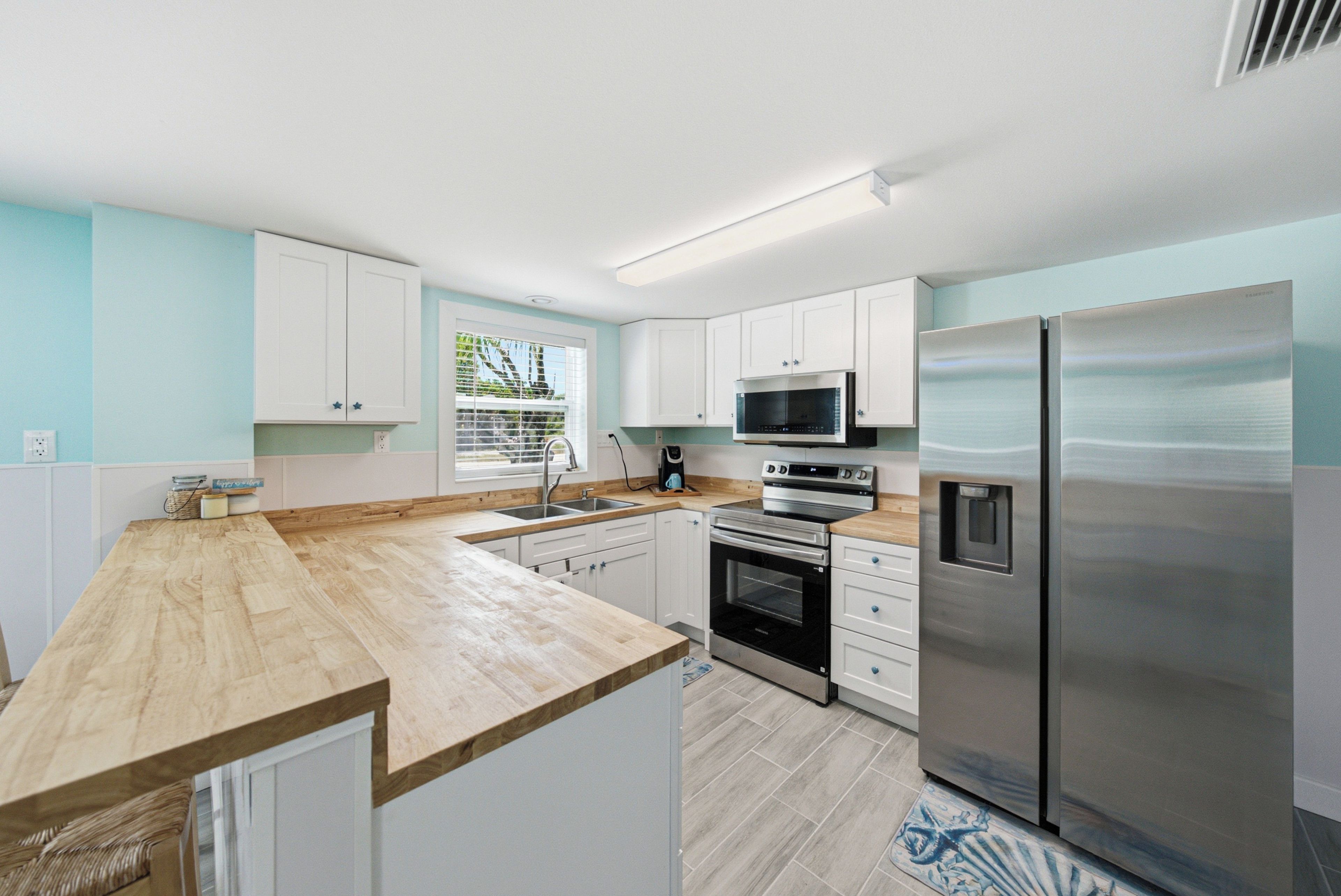 A modern kitchen with white cabinets, a stainless steel refrigerator, a microwave, and an oven.