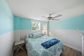 Un dormitorio con cama, ventilador, ventana y mesita de noche.