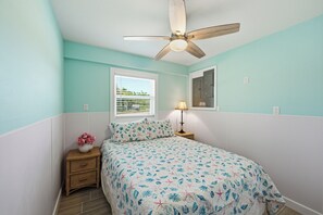 Un dormitorio con cama, mesita de noche, lámpara, ventana y ventilador de techo.