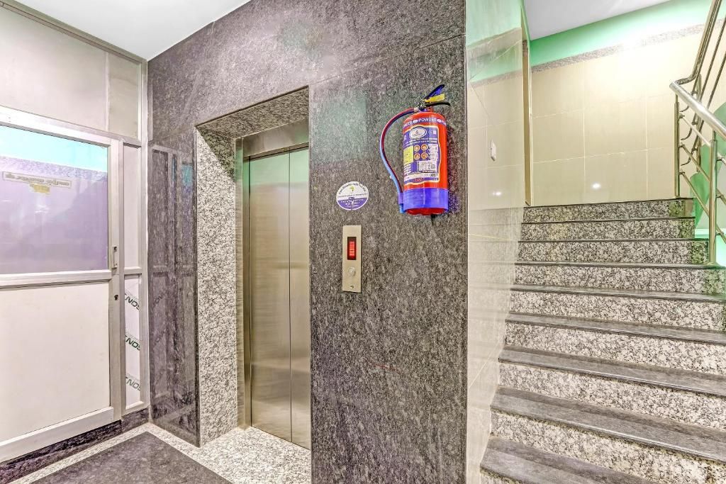 An elevator with a fire extinguisher mounted on the wall, a control panel, and a staircase with a handrail.