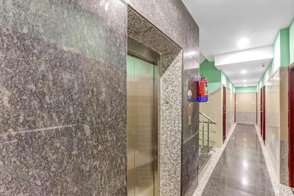 A hallway with a marble wall, a fire extinguisher mounted on the wall, and a door with a metallic handle.