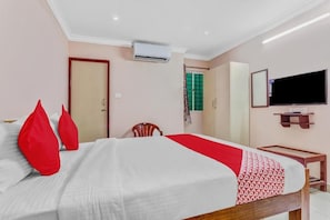 Quarto de hotel com cama, televisão, guarda-roupa e janela vista para o verde.