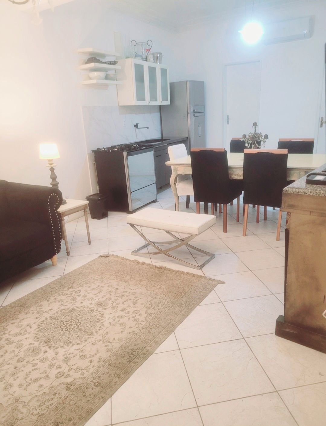 Una sala de estar con un sofá, una mesa de comedor con sillas, una zona de cocina con armarios y una alfombra en el suelo.